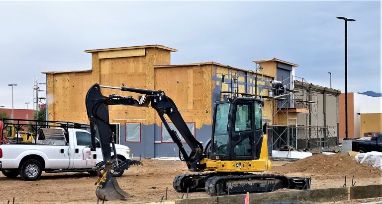 A compact excavator and a work truck on a commercial construction site